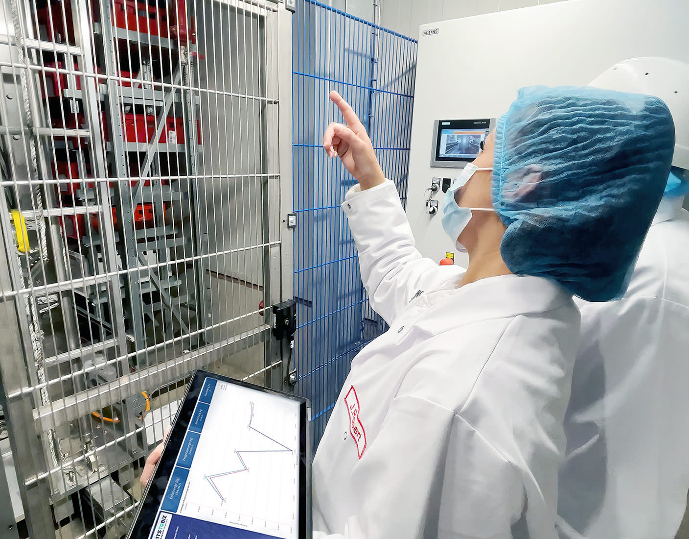 Two scientists in lab coats focused on a tablet in a food production environment.